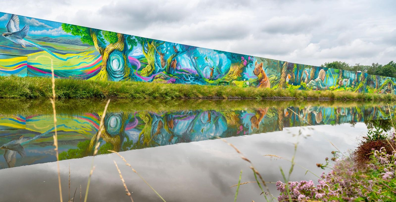 Een lange kleurrijke muurschildering weerspiegeld in het water van het kanaal